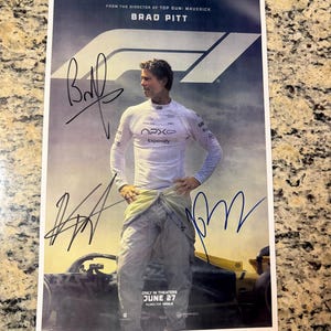 Könnte beinhalten: Ein Filmplakat mit Brad Pitt in einem Rennanzug, mit dem F1-Logo und Unterschriften. Das Plakat wirbt für den Film "From the Director of Top Gun: Maverick". Der Text "ONLY IN THEATERS JUNE 27" ist ebenfalls sichtbar.