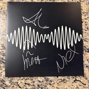 May include: A square black vinyl record jacket featuring a white sound wave graphic centered horizontally. The cover is signed in silver ink with four distinct autographs positioned above and below the central white waveform design.