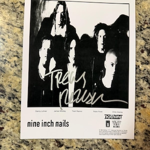 May include: Black and white photograph of the band Nine Inch Nails. The band members are in a group, with the band's name and member names at the bottom. The photograph is signed by Trent Reznor.
