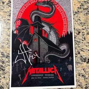 May include: A rectangular concert poster featuring a black dragon coiled around a church building against a large red circular background. The text reads METALLICA COPENHAGEN DENMARK June 16 2024 Parken Stadium. A white signature is visible on the left side.