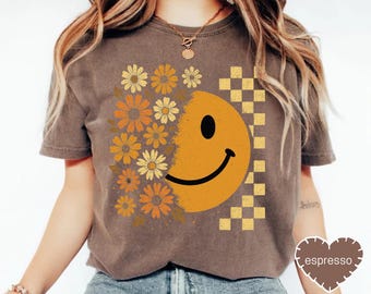 May include: Brown t-shirt featuring a large yellow smiley face design. The design incorporates a floral pattern on one side and a checkered pattern on the other. The word "espresso" is on the bottom right.