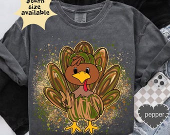 May include: Dark gray sweatshirt featuring a cartoon turkey with a peace sign. The turkey has brown, green, and yellow feathers and a matching hat. The text "Youth size available" is in a yellow starburst. The word "pepper" is on a heart.