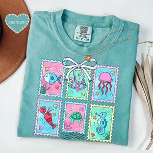 A turquoise t-shirt with a colorful graphic design of various sea creatures, including fish, jellyfish, and sea creatures, arranged in a grid-like pattern.