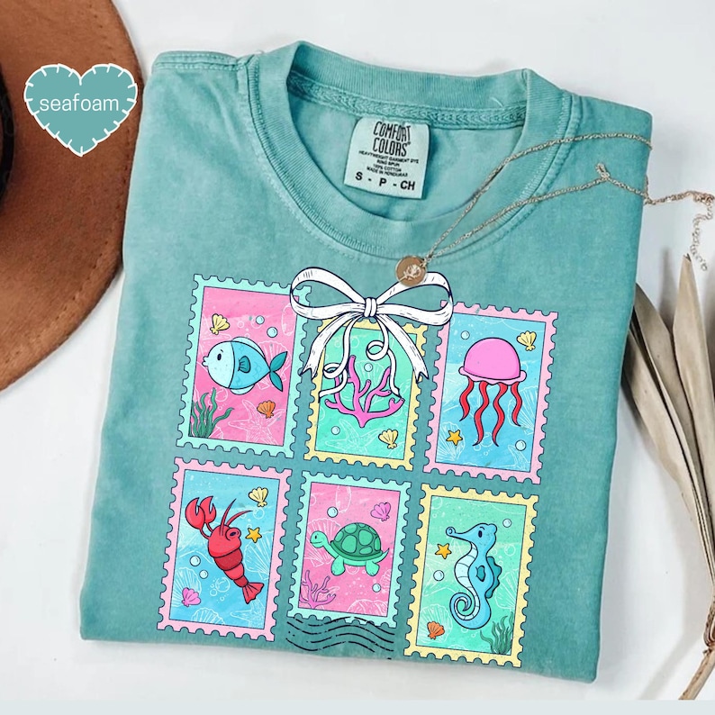 A turquoise t-shirt with a colorful graphic design of various sea creatures, including fish, jellyfish, and sea creatures, arranged in a grid-like pattern.