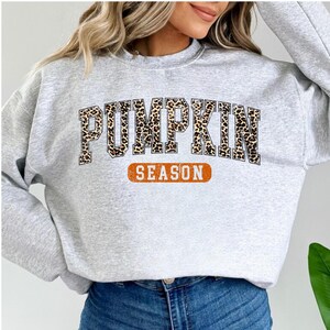A woman wearing a grey sweatshirt with the word "PUMPKIN" printed on it, along with the word "SEASON" below it.