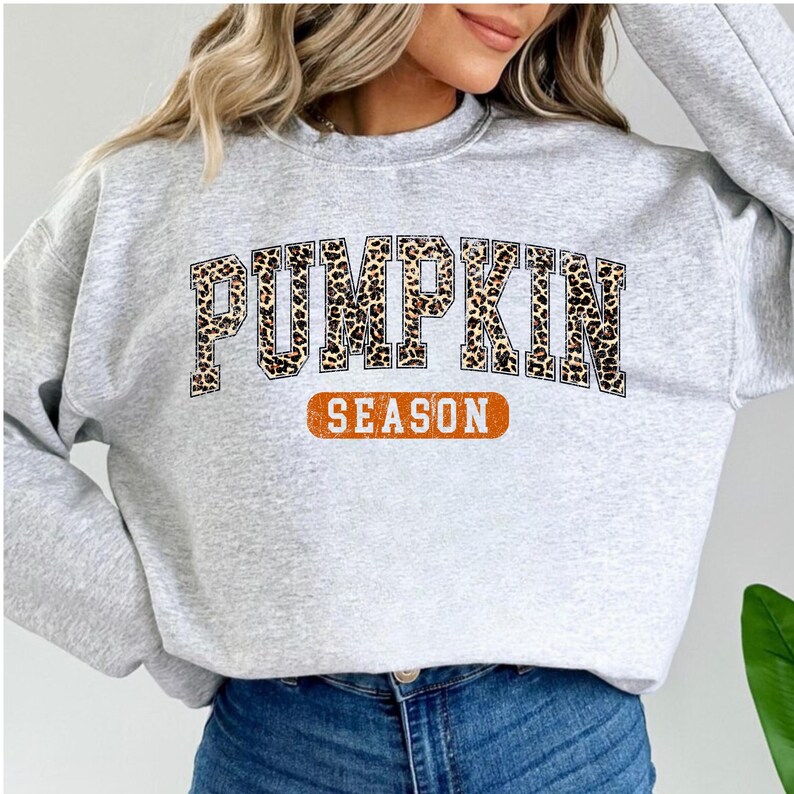 A woman wearing a grey sweatshirt with the word "PUMPKIN" printed on it, along with the word "SEASON" below it.