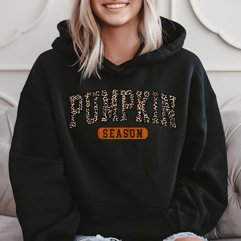 A woman wearing a black hoodie with the word "PUMPKIN" printed on it, sitting on a couch.