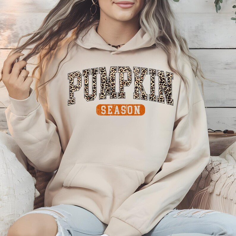 A woman wearing a beige hoodie with the word "PUMPKIN" printed on it, sitting on a couch.