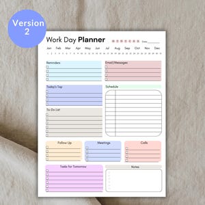 K&ouml;nnte beinhalten: Ein wei&szlig;er Work Day Planner mit farbigen Abschnitten f&uuml;r Erinnerungen, To-Do-Listen und Terminplanung. Der Planer enth&auml;lt Abschnitte f&uuml;r E-Mails, Besprechungen und Anrufe. Der Text "Version 2" befindet sich in einem blauen Kreis.