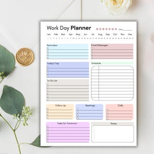K&ouml;nnte beinhalten: Ein wei&szlig;er Work Day Planner mit Abschnitten f&uuml;r Erinnerungen, E-Mails, Aufgaben und einen Zeitplan. Der Planer hat ein Pastellfarbschema und enth&auml;lt die Wochentage und Monate des Jahres. Ein goldenes Wachssiegel und Gr&uuml;nzeug befinden sich im Hintergrund.