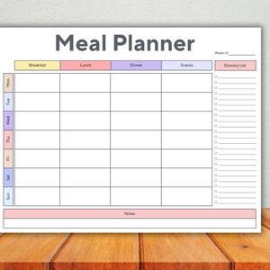 Op de afbeelding: Een witte maaltijdplanner met de titel "Meal Planner" in grijs. De planner heeft secties voor ontbijt, lunch, diner en snacks, met een boodschappenlijst aan de rechterkant.