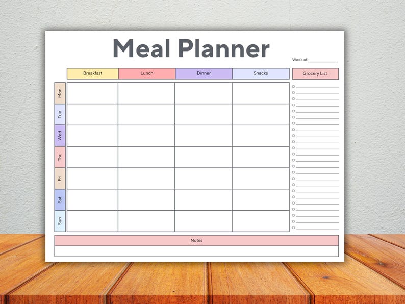 Op de afbeelding: Een witte maaltijdplanner met de titel "Meal Planner" in grijs. De planner heeft secties voor ontbijt, lunch, diner en snacks, met een boodschappenlijst aan de rechterkant.