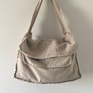 May include: A beige canvas tote bag with a frayed edge and a single strap. The bag has a folded over top with a textured fabric.