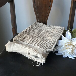May include: A beige fabric cushion with a textured surface. The cushion is folded and placed on a dark brown chair.