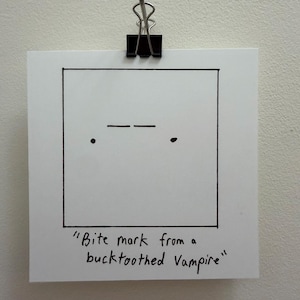 Puede incluir: Una tarjeta cuadrada blanca con un dibujo sencillo en tinta negra de dos líneas horizontales y dos puntos, con el texto escrito a mano "Bite mark from a bucktoothed Vampire" debajo del dibujo. La tarjeta está sujeta por un clip metálico negro.