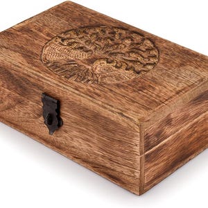 May include: A rectangular wooden box with a carved tree of life design on the lid. The box is made of a warm brown wood and features a dark metal clasp. The wood grain is visible, adding to the rustic aesthetic.