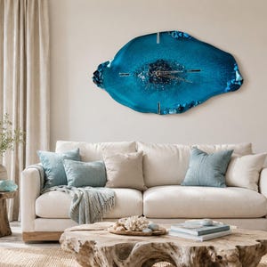 May include: A large, irregular, geode-inspired wall clock featuring a deep blue and teal resin finish with embedded crystals and metallic hands. The clock has a glossy, organic shape with textured edges and a dark, shimmering center point.