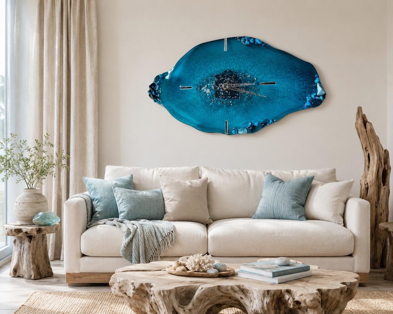 May include: A large, irregular, geode-inspired wall clock featuring a deep blue and teal resin finish with embedded crystals and metallic hands. The clock has a glossy, organic shape with textured edges and a dark, shimmering center point.
