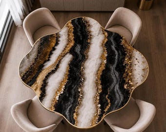May include: A flower-shaped dining table with a surface featuring swirling patterns of black, white, and metallic gold. The table is surrounded by four beige upholstered chairs with curved backrests, arranged symmetrically around the central piece.