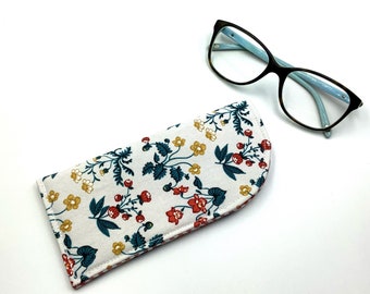 May include: A white fabric glasses case with a floral pattern featuring red, yellow, and blue flowers. The case is lying on a white surface next to a pair of blue-tinted glasses with black frames.