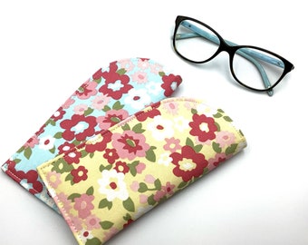 May include: Two floral patterned eyeglass cases. One case is light blue with pink and white flowers. The other case is yellow with pink and red flowers.
