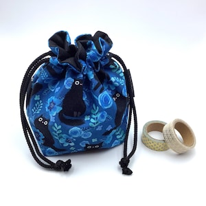 May include: A blue drawstring bag featuring a black cat and floral design. The bag has a black drawstring closure and is accompanied by two rolls of decorative tape. The bag is approximately 15 cm tall.