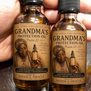 May include: Two amber glass dropper bottles labeled Grandma's Protection Oil Psalm 23. The label features an illustration of an elderly person, the text The Lord is my shepherd I shall not want, and the maker name Madam C Oracle in black ink.