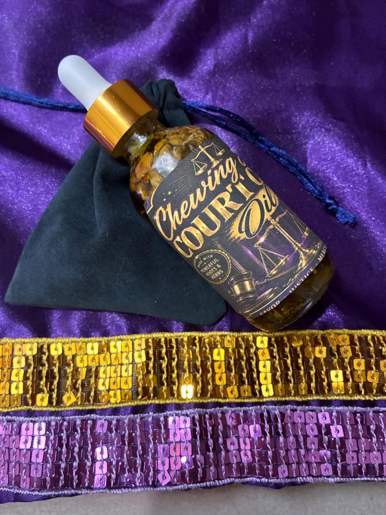 May include: A glass bottle with a dropper, filled with a golden liquid and herbs, labeled "Chewing Court Oil." The bottle rests on a purple cloth with a black pouch and gold and purple sequin trim. The label features scales of justice.
