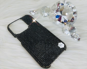 Puede incluir: Funda de teléfono negra cubierta de pequeños diamantes de imitación negros con un logotipo plateado que dice "Bling" y "Dubai".