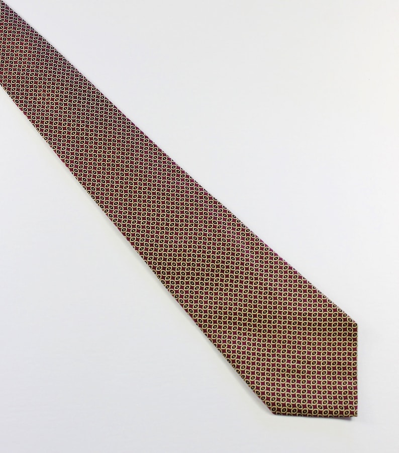 May include: A red tie with a gold and black geometric pattern.