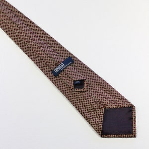 May include: A burgundy silk tie with a gold geometric pattern. The tie has a navy blue label that reads "Polo by Ralph Lauren".
