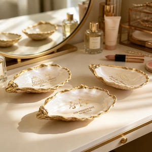 May include: Three white oyster shell trinket dishes with gold-painted edges. One dish features a gold cake illustration with the text "Jack & Annie". Another shows two gold rings with "Jack & Annie 08.08.2026". The third displays "Jack & Annie" and "OUR WEDDING DAY 08.08.2026".