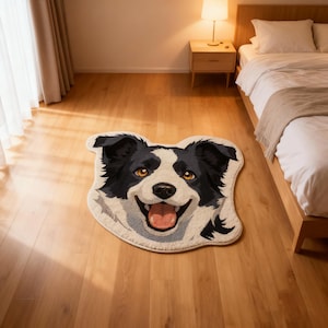 May include: A rug shaped like a smiling Border Collie dog's face. The rug features black and white fur with tan eyes and a pink tongue. The rug is on a hardwood floor in a bedroom.