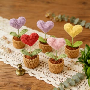 May include: Six crocheted heart-shaped flowers in small brown pots. The hearts are in shades of purple, red, pink, and yellow. Each flower has green leaves and sits in a crocheted pot, giving a charming, handmade appearance.