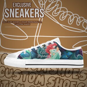 Pu&ograve; includere: Scarpe da ginnastica in tela bianca con un design colorato de "La Sirenetta". Le scarpe hanno un profilo basso con lacci bianchi e una suola in gomma. Il design include il testo "EXCLUSIVE SNEAKERS" e "CUSTOM SHOES".