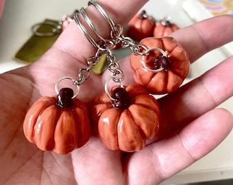 May include: Orange pumpkin keychains with silver metal rings and chains. The miniature pumpkins have a ribbed texture and a dark brown stem. Several keychains are visible, suggesting a seasonal or autumn theme.