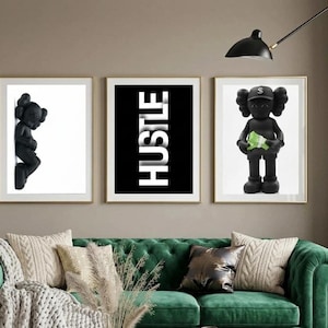 May include: Three framed art prints. The left print features a black figurine on a white background. The center print has the word "HUSTLE" in white on a black background. The right print shows a black figurine holding green money. The prints are above a green sofa.