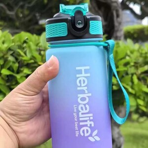 May include: A blue and purple water bottle with a teal lid and a black strap. The bottle has the Herbalife logo and the text "Live your best life".