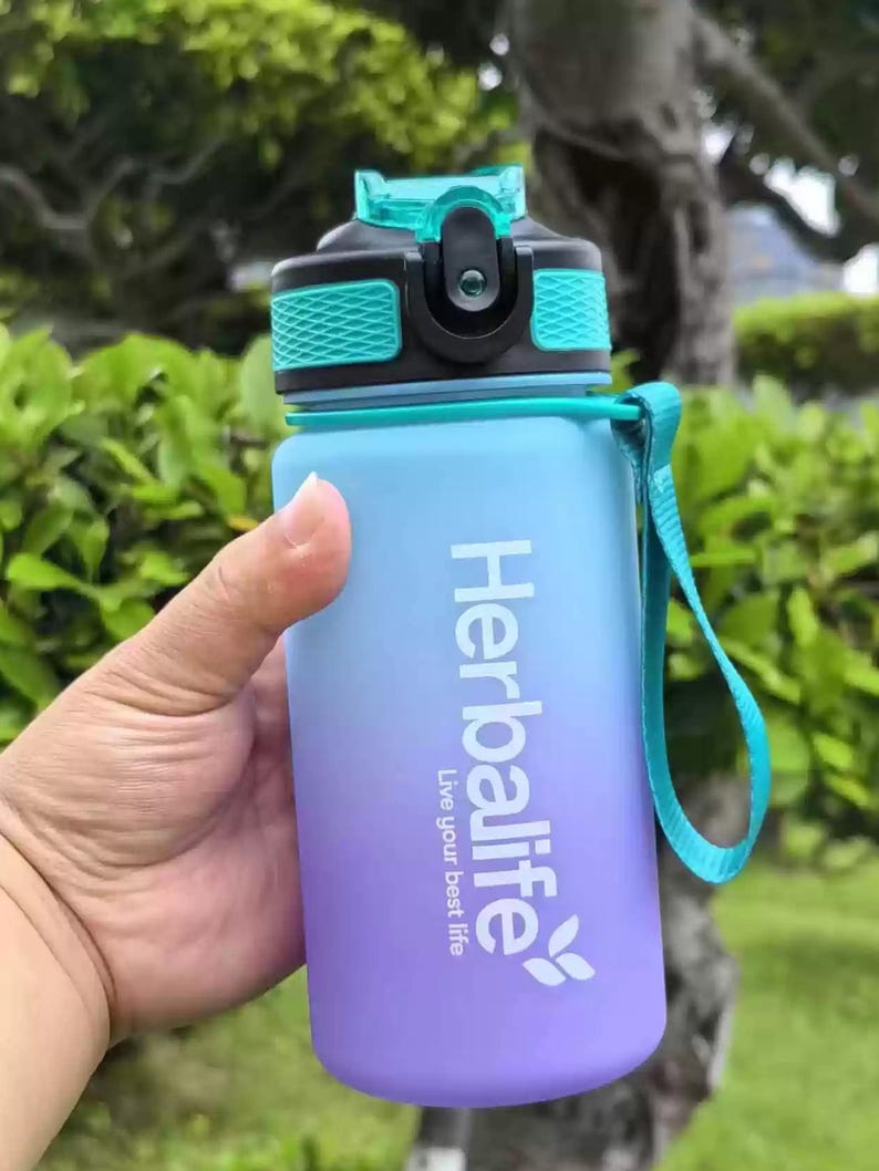 May include: A blue and purple water bottle with a teal lid and a black strap. The bottle has the Herbalife logo and the text "Live your best life".