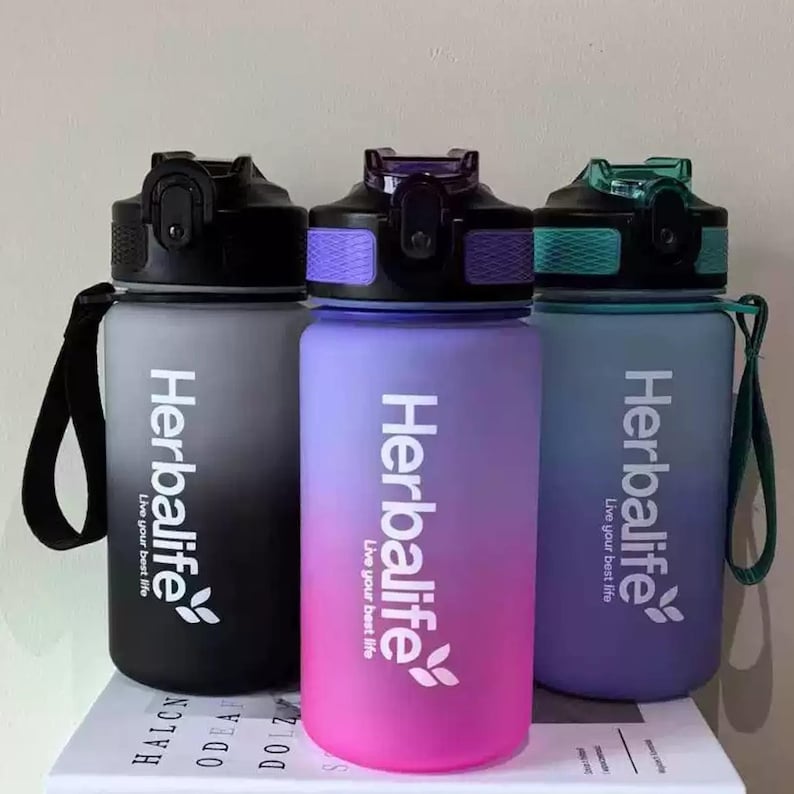 May include: Three water bottles with a gradient design. The bottles are black, pink, and purple with the Herbalife logo and the text "Live your best life".