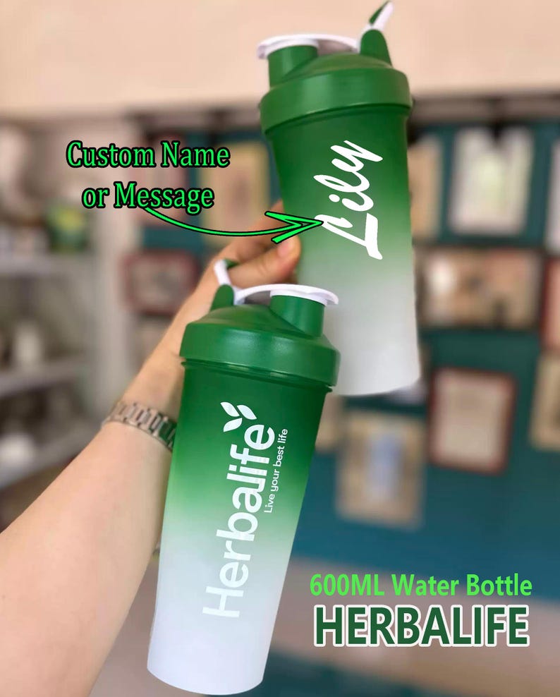 Puede incluir: Dos botellas de agua con degradado verde y blanco. Una botella tiene el nombre "Lily" en escritura blanca. La otra botella tiene el logotipo y el texto "Herbalife". Las botellas est&aacute;n etiquetadas como "600ML Water Bottle" y "Custom Name or Message".