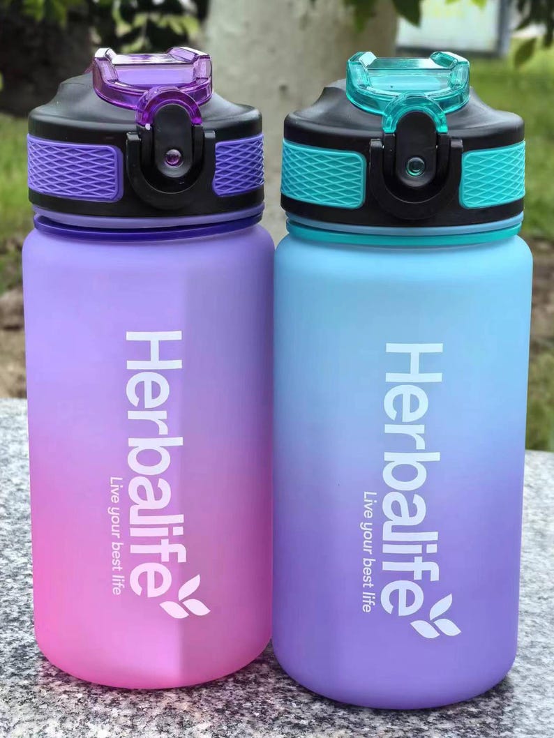 May include: Two ombre water bottles with black lids and purple and blue color gradients. The bottles have the Herbalife logo and the text "Live your best life" printed on them.