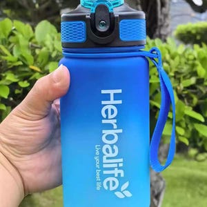 May include: Blue and black water bottle with a blue and black lid and a blue carrying strap. The bottle has a white Herbalife logo with the text "Live your best life".