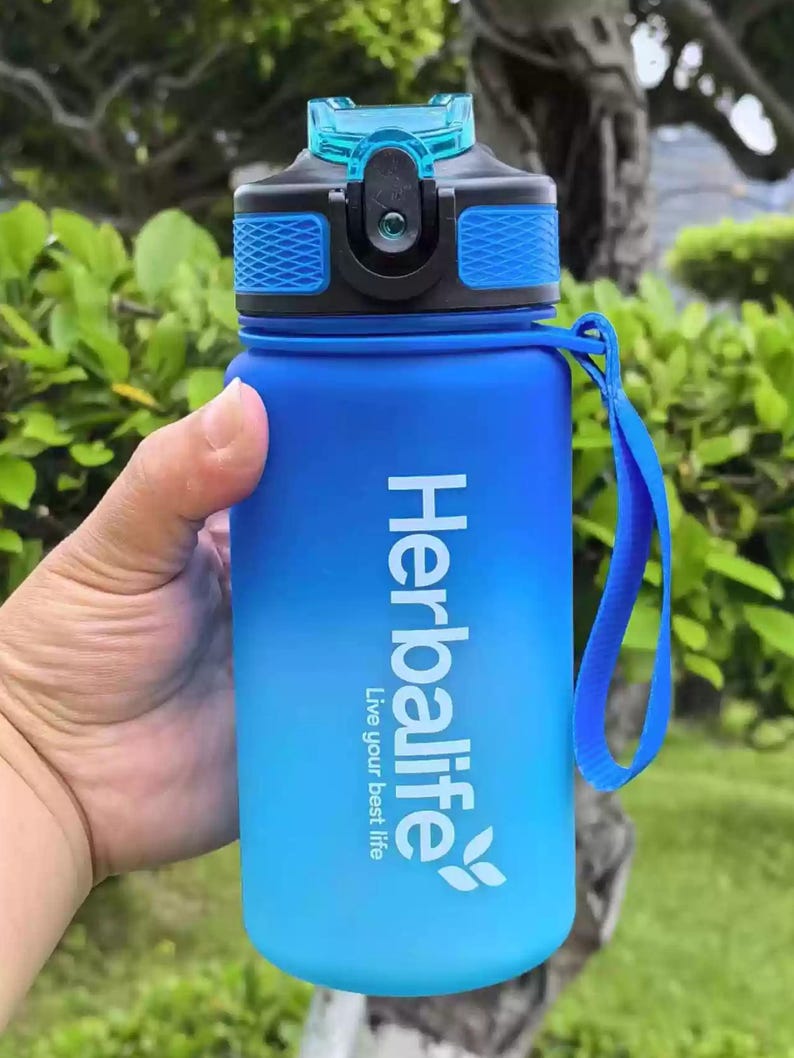 May include: Blue and black water bottle with a blue and black lid and a blue carrying strap. The bottle has a white Herbalife logo with the text "Live your best life".