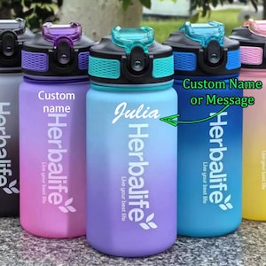 May include: Five colorful water bottles with a gradient design. Each bottle has a different name or message on it, including "Julia", "Custom name", and "Custom Name or Message". All bottles have the Herbalife logo and the phrase "Live your best life".