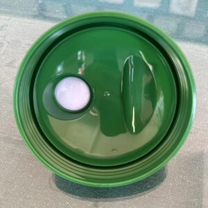 Puede incluir: Vista superior de una tapa de pl&aacute;stico verde con un bot&oacute;n blanco y una abertura curva. La tapa es de color verde vibrante y tiene un acabado brillante. El bot&oacute;n blanco es circular y ligeramente elevado.