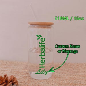 May include: A clear glass tumbler with a bamboo lid and a glass straw. The tumbler has the word "Herbalife" in green, along with the name "Lily". The tumbler holds liquid and is labeled 16oz / 510ML. The text "Custom Name or Message" is also visible.