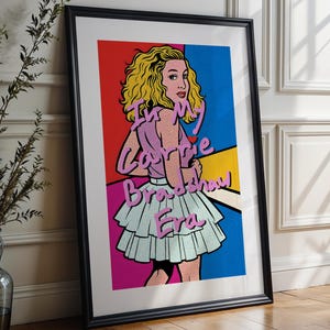 May include: A framed pop art print depicting a woman with blonde curly hair, wearing a pink top and a light blue skirt. The artwork has a comic book style with the text "My Carrie Broadway Era" in pink. The background is divided into red, blue, and yellow sections.
