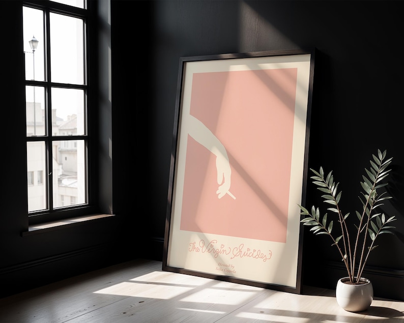 Peut inclure: Une affiche encadr&eacute;e avec un fond rose et une silhouette blanche d'une main tenant une cigarette. Le texte "The Virgin Suicides" est imprim&eacute; en cursive au bas de l'affiche.