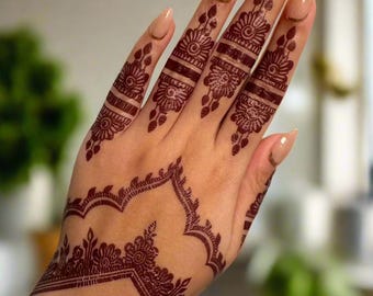 May include: A close-up of a hand with intricate henna designs on the fingers and wrist. The henna is a deep maroon color and the design features floral and geometric patterns.